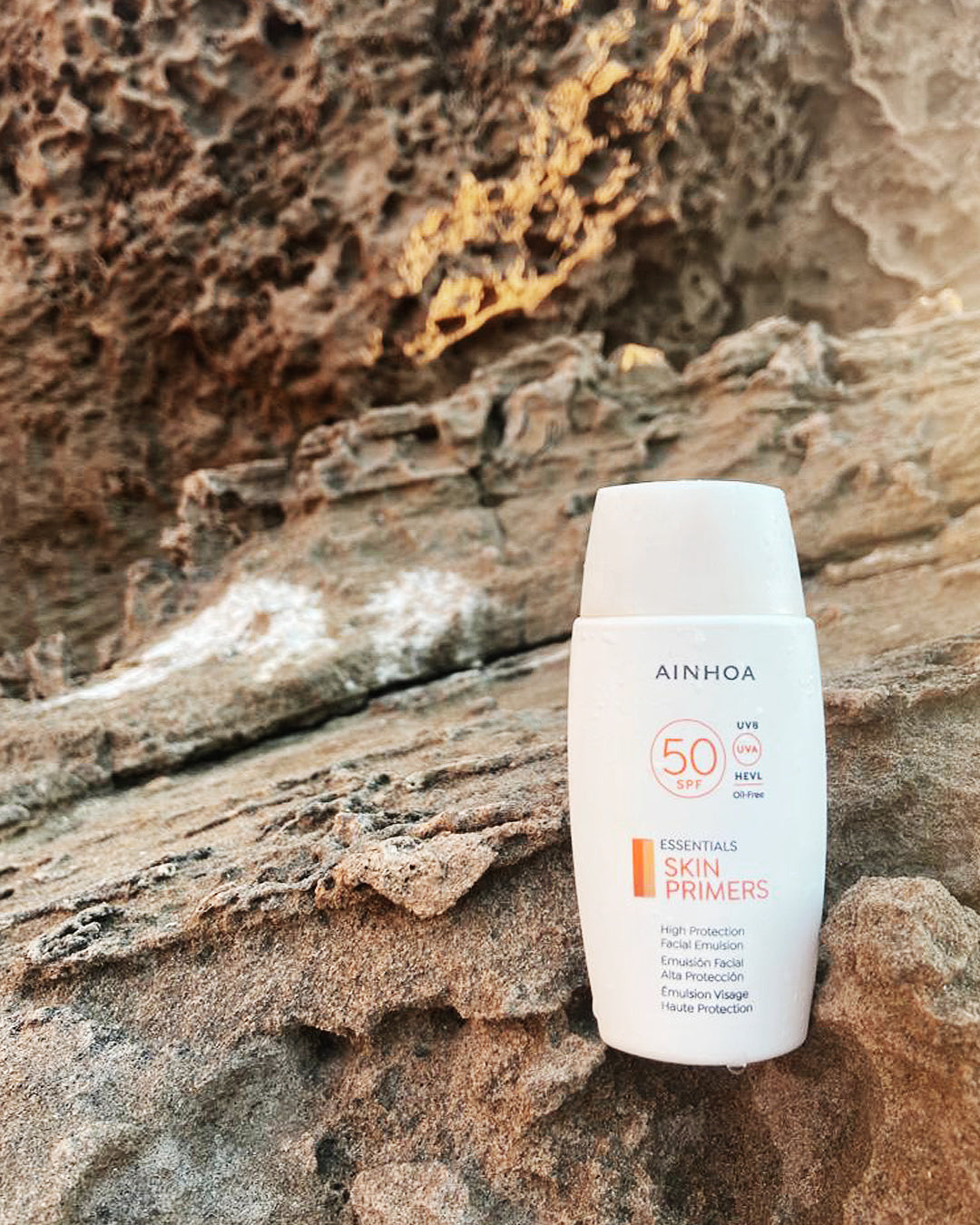Billedet viser hudplejeproduktet Ainhoa SPF 50 ansigtsemulsion: Vegansk, parfumefri og oliefri. Mikroplastfri og silikonefri, skånsom og marinevenlig, og som står på en klippe.