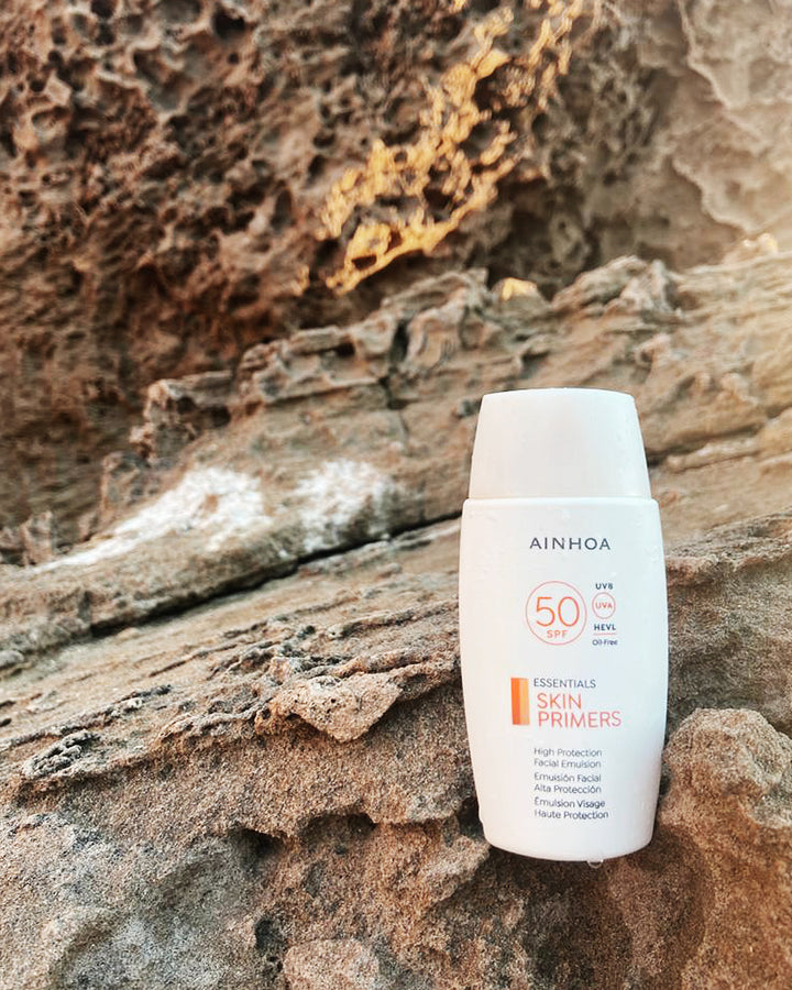 Billedet viser hudplejeproduktet Ainhoa SPF 50 ansigtsemulsion: Vegansk, parfumefri og oliefri. Mikroplastfri og silikonefri, skånsom og marinevenlig, og som står på en klippe.