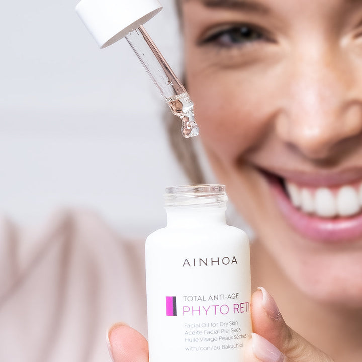 Billedet viser en kvinde der holder en ansigtsolie i hånden og drypper oliedråber fra Ainhoa Phyto Retin+ Facial Oil ned i flasken. Ansigtsolien er vegansk og kraftigt opstrammende olie med bakuchiol for tør og meget tør hud. Nærer, fugter og reducerer rynker.