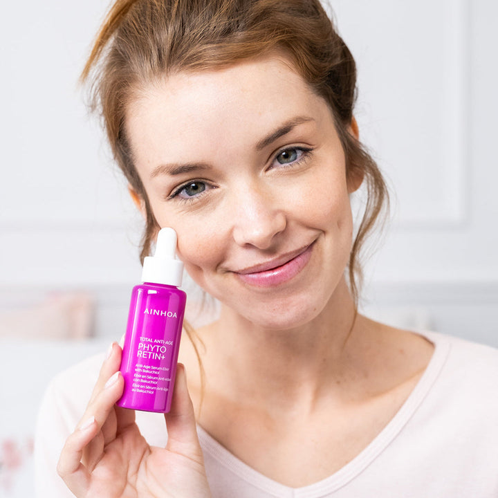 Smilende kvinde der holder hudplejeproduktet Ainhoa Anti-Age Serum Elixir: Kraftigt opstrammende, nærende anti-age serum med bakuchiol, baobabolie og tranebærekstrakt. Klinisk testet.