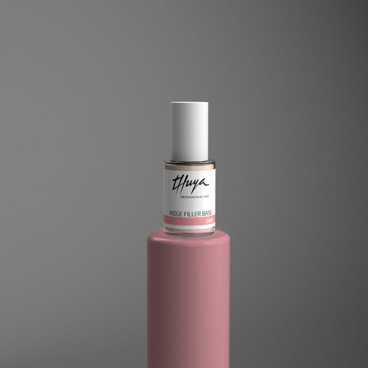 Billedet viser negleproduktet Thuya Ridge Filler Base Nail Care, som er en lufttørrende basecoat, der er designet til at forbedre neglens udseende øjeblikkeligt. Denne basecoat udfylder omgående riller og skjuler eventuelle ujævnheder, hvilket giver en glat og jævn overflade, klar til lakering eller en naturlig finish. Negleproduktet er opstillet på et lyserødt piedestal der symboliserer Thuyas farvekoder for korrekt neglebehandling.
